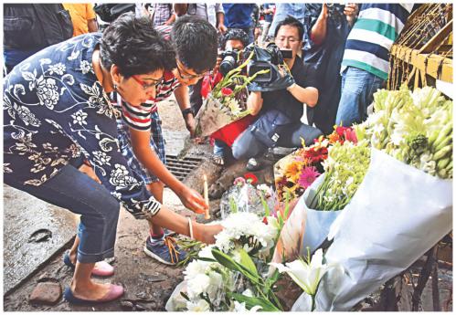 An Indian lady placing wreaths at the road block leading to the restaurant. Next to her, a boy putting a candle at the vigil. Photo: Star
