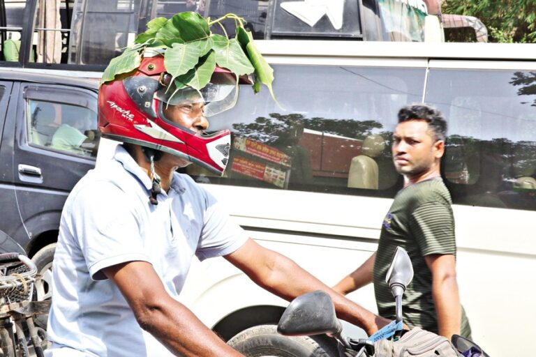 バイクに乗った男性が、涼をとるためにヘルメットの上にガジュマルの葉を置いている。