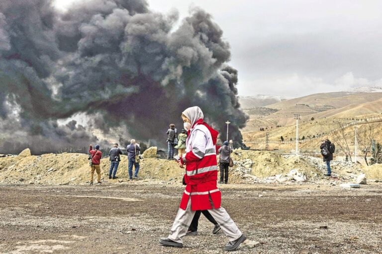 イラン赤新月社の女性会員が煙の近くを歩く